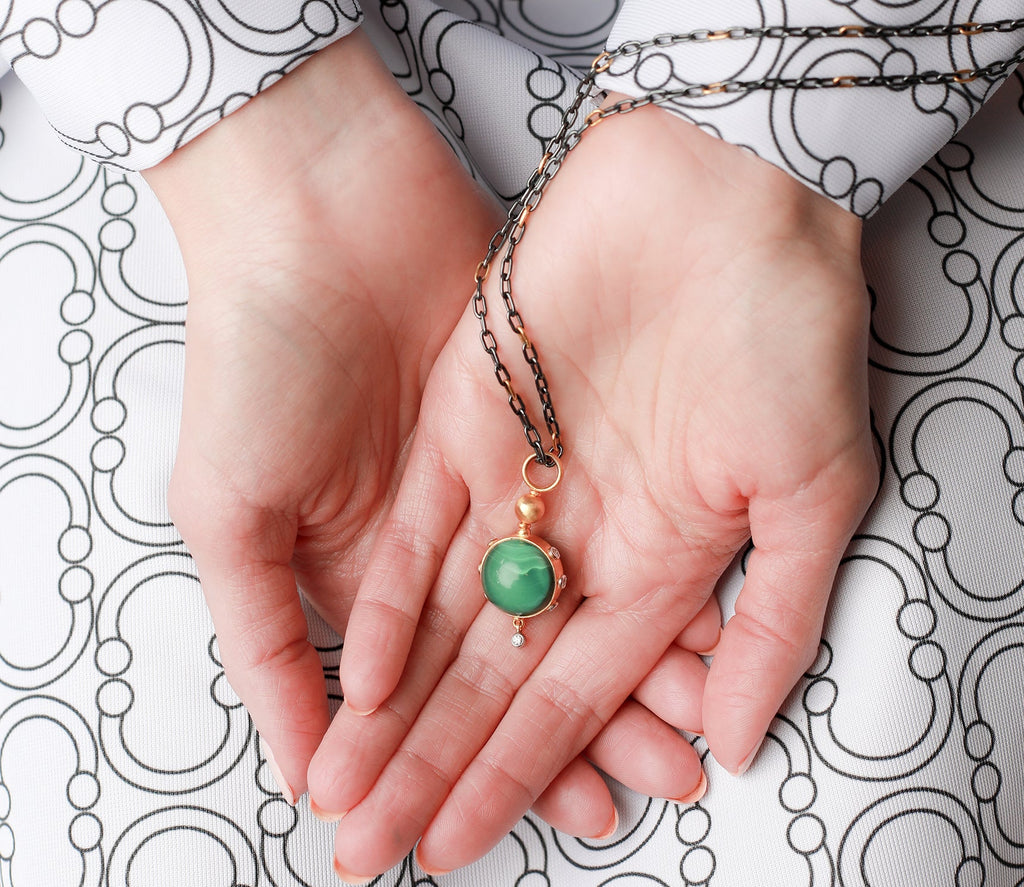 Person holding a necklace with a green pendant on a patterned background