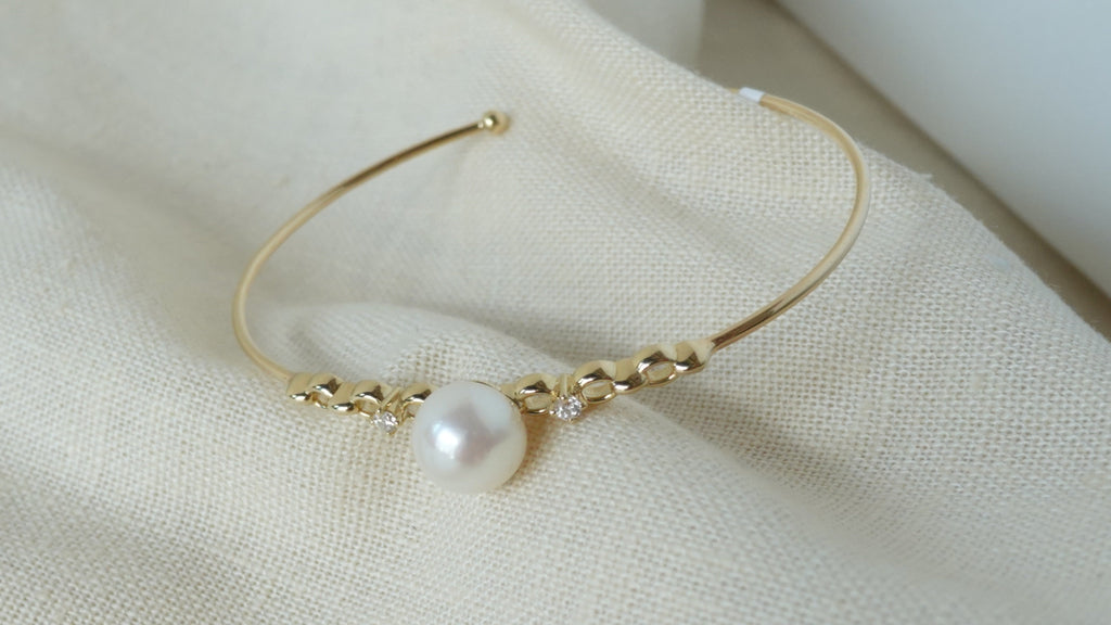 Gold bracelet with a pearl on a beige fabric background